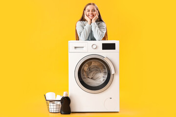 Pretty young woman leaning on washing machine on yellow background - obrazy, fototapety, plakaty