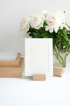 Folio photo frame in a wooden holder with a bouquet of peonies on the background