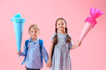 Happy little classmates with backpacks and colorful school cones on pink background