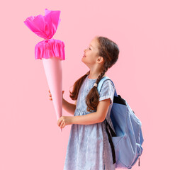 Happy little girl with backpack and school cone on pink background