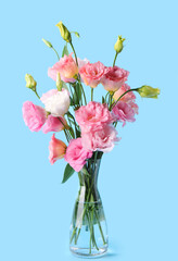 Glass vase with beautiful pink eustoma flowers on blue background