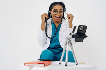 Happy african american doctor woman wears medical coat holding and using smartphone with digital...