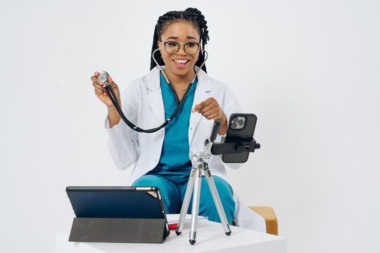 Happy African American Doctor Woman Wears Medical Coat Holding And Using Smartphone With Digital Tablet Against White Background