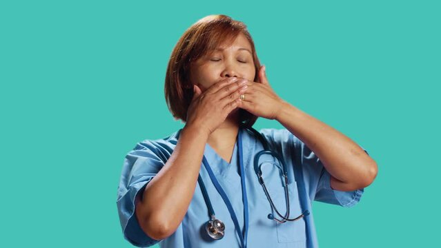 Certified nurse covering mouth with hands, holding back from saying rude thoughts. Hospital employee silencing herself, abstaining from speaking, isolated over studio background, close up