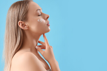 Pretty young woman with heart made of cream on her face against blue background