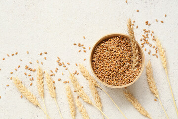 Wooden bowl with wheat ears and grains on white table
