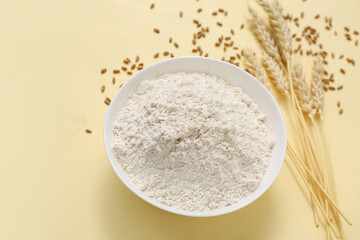 Bowl with wheat flour and spikelets on yellow background