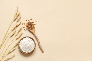 Wheat flour in bowl, spoon with grains and spikelets in beige background