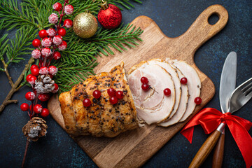 Christmas baked ham sliced with red berries and festive decorations on wooden cutting board, dark rustic background from above. Christmas and New Year holiday dinner with baked pork - obrazy, fototapety, plakaty
