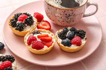 Plate of tasty tartlets with whipped cream and berries on pink tile background