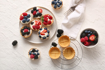 Plate of tasty tartlets with whipped cream and berries on white background