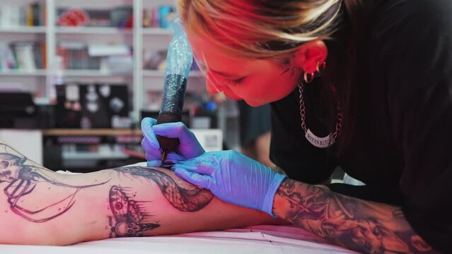 Tattoo artist doing tattoo on client leg in salon closeup tattoo making process. High quality 4k footage