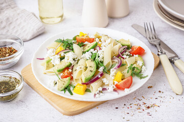 Plate of tasty pasta salad with tomatoes and avocado on white background