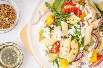 Plate of tasty pasta salad with tomatoes and avocado on white background