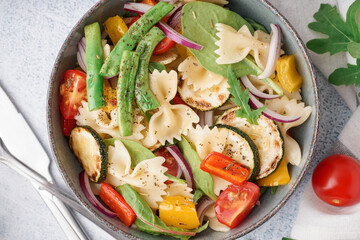 Bowl of tasty pasta salad with pepper and tomatoes on white background