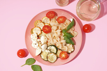 Plate of tasty pasta salad with tomatoes and basil on pink background