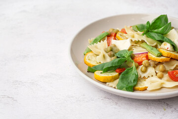 Plate of tasty pasta salad with peas and basil on white background