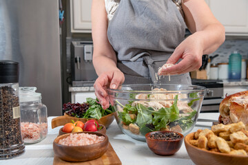 Cooking Caesar salad. Cook adds grated parmesan to glass bowl with salad in a home kitchen.
