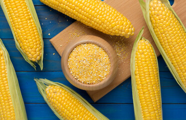 Corn groats with fresh cobs on wooden background, top view