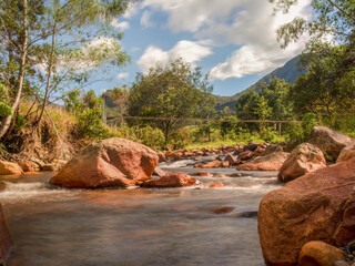 Long-exposure photography of the stream an the rocks of the El Valle river, with a rustic hanging bridge, in the eastern Andean mountains of central Colombia, near the town of Arcabuco.