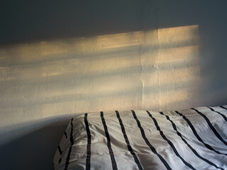 The shadow of a window frame and the light of the sunset above a bed untidy covered with a black striped white duvet.