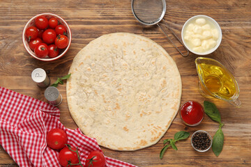 Pizza crust and ingredients on wooden background