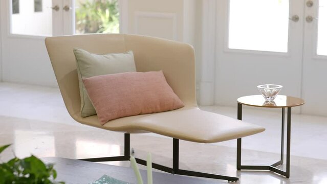 Close up view of comfy design leather chair with two soft pastel pillows and small coffee table places in bright living room. Domestic place for relaxation