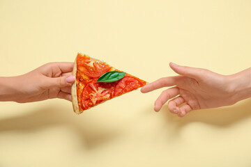Female hands with slice of tasty pizza on yellow background