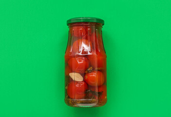 Jar with canned tomatoes on green background