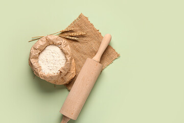Bag of flour, rolling pin and wheat ears on green background