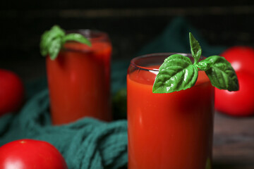 Glass of tasty tomato juice on black wooden background