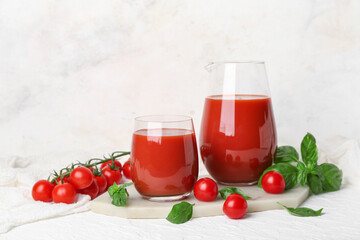 Glass and jug of tasty tomato juice on white background
