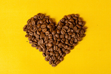 heart shaped high roasted coffee bean with old yellow alarm clock on yellow isolated background, coffee time(hora do café)