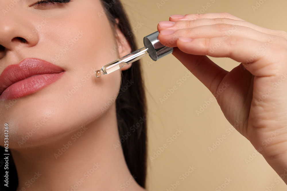 Wall mural Young woman applying essential oil onto face on beige background, closeup