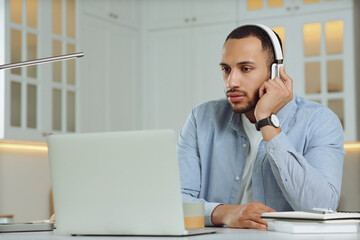 Obraz premium Young man with headphones working on laptop at desk in kitchen. Home office