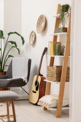 Spring atmosphere. Wooden shelving unit, acoustic guitar and comfortable chair in stylish room