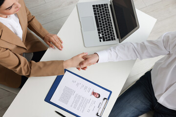 Human resources manager shaking hands with applicant during job interview in office, top view