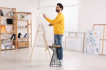 Man painting in studio. Using easel to hold canvas