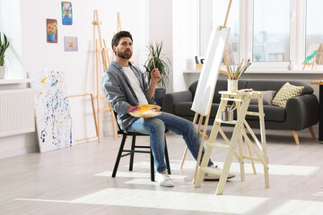 Man painting in studio. Using easel to hold canvas