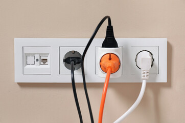 Many different electrical power plugs in sockets on beige wall