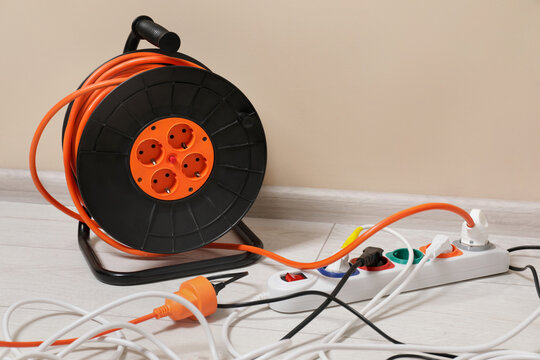 Extension cord reel plugged into socket on white floor indoors, space for text. Electrician's equipment