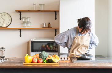 料理中に体調不良になるエプロン姿の女性・主婦（腰痛）
