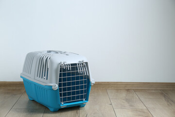 Light blue pet carrier on floor near white wall. Space for text