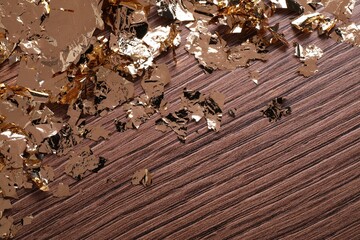 Many pieces of edible gold leaf on wooden table, top view. Space for text