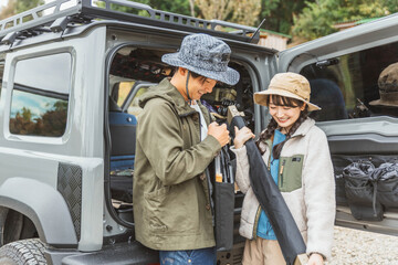 秋冬のアウトドア・キャンプ場にキャンプに来て車の荷台から荷物を運ぶ仲間達（男女・アジア人）
