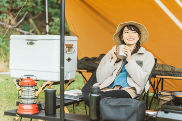 キャンプ場でソロキャンプする若い女性キャンパー（飲む）
