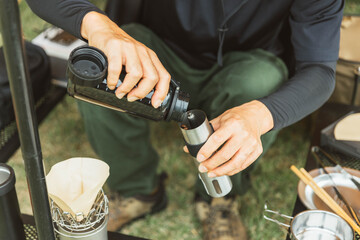 キャンプ場でコーヒーミルにコーヒー豆を入れる男性キャンパー
