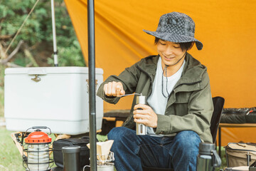 キャンプ場でソロキャンプする若い男性キャンパー（コーヒーミル）
