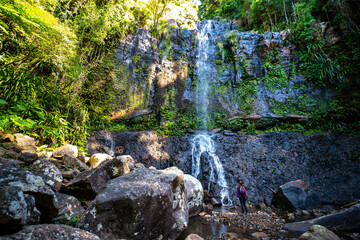 A beautiful girl stands in front of a tall, powerful waterfall; hike in Gondwana Rainforest on the Warrie Circuit trail in Springbrook National Park, Gold Coast, Queensland