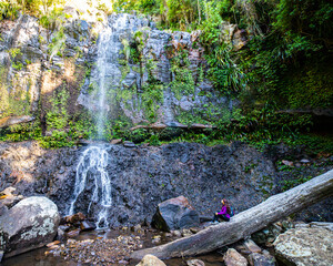 A beautiful girl sits in front of a stunning, powerful waterfall; hike in Gondwana Rainforest on the Warrie Circuit trail in Springbrook National Park, Gold Coast, Queensland	